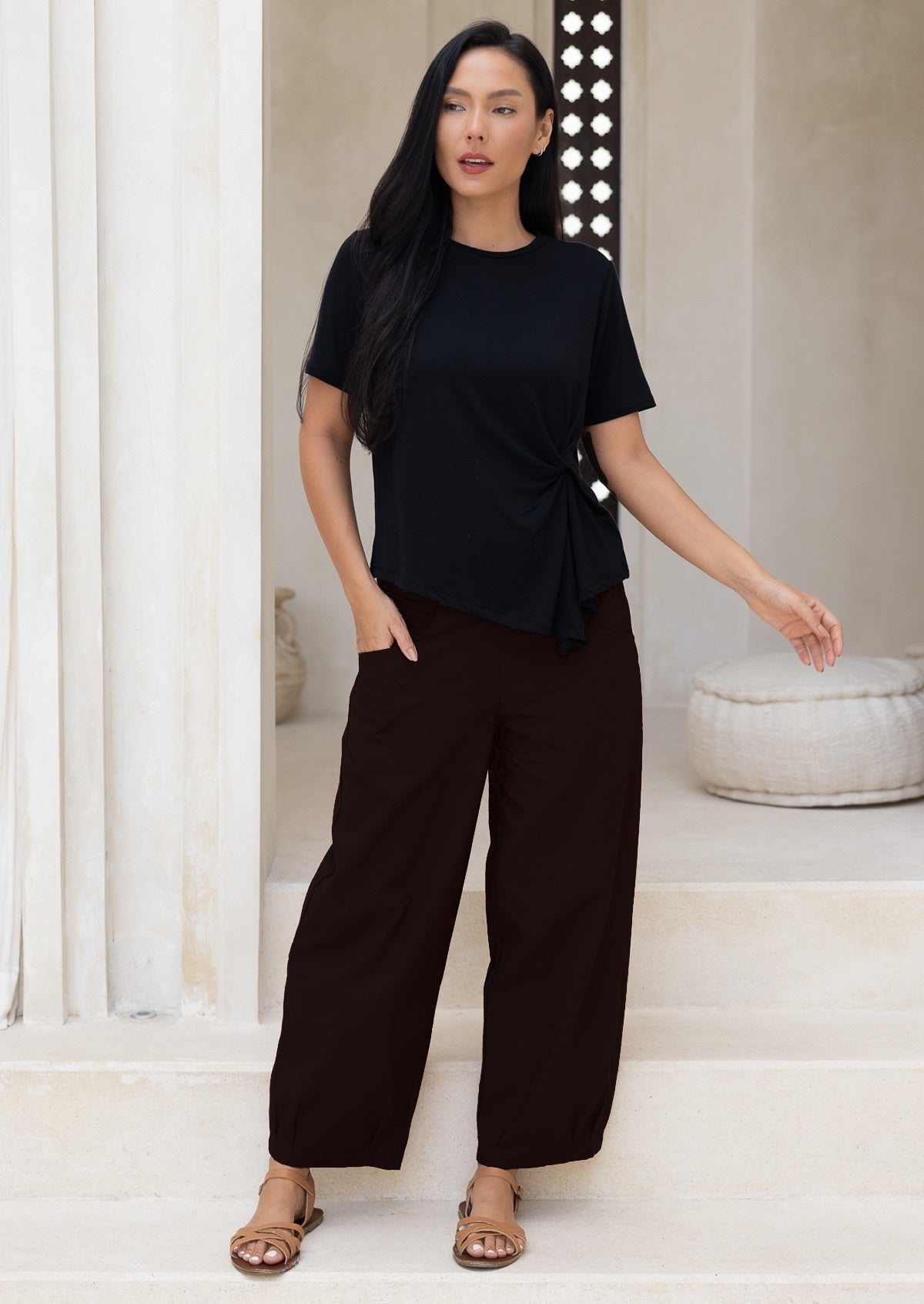 Woman wearing a black wide legged cotton pants standing
minimalistic room.