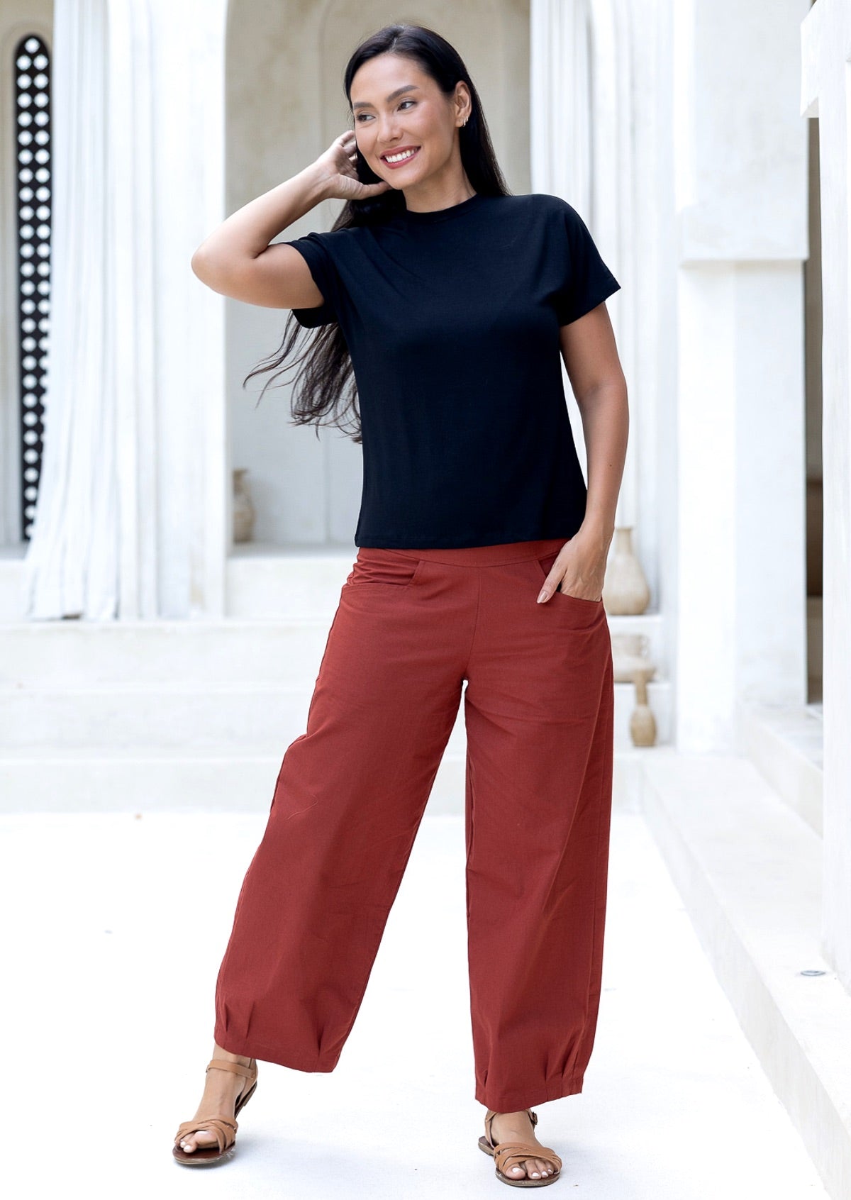 Model poses in burnt henna relaxed fit cotton pants with pockets, side zipper and pleated ankles