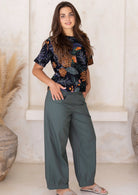 Model posing in a jungle green 100 percent cotton pants, paired with a black floral printed top