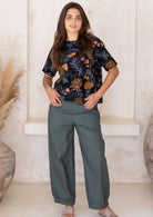 Woman wearing a green wide leg cotton pants with pockets and black floral top in a minimalistic setting