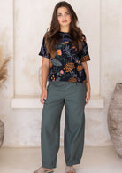 Woman wearing a green 100% cotton wide leg tapered pants with pleats at the ankles and pockets.