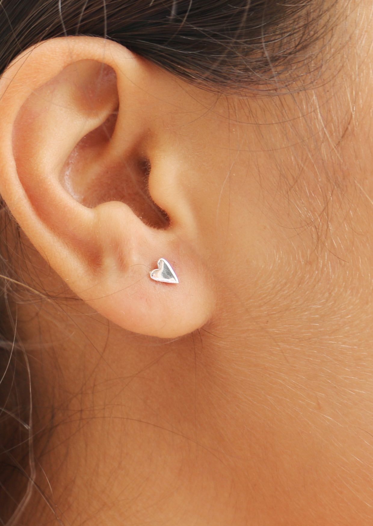 Close-up image of a person wearing elongated silver heart shaped studs