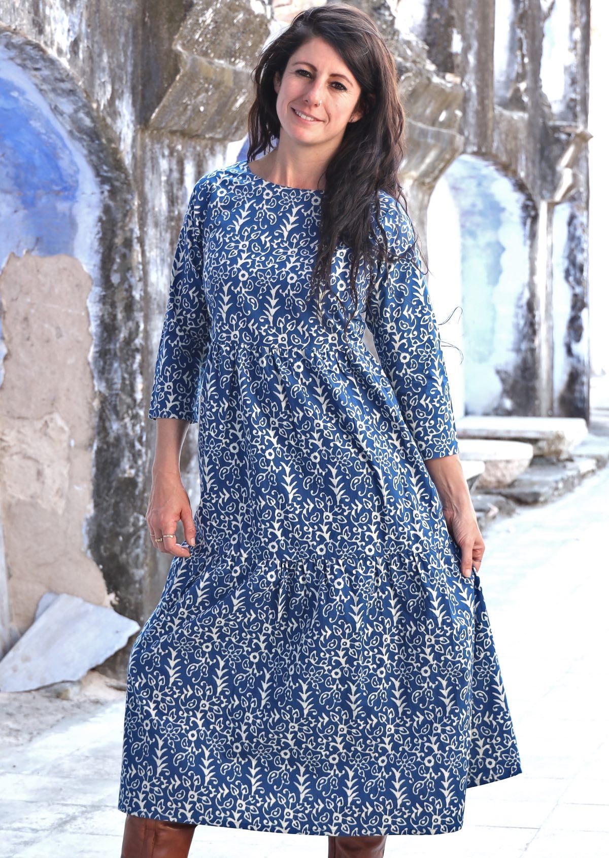 Model with dark hair wearing a blue cotton three tiered midi length dress with blue base and white floral print