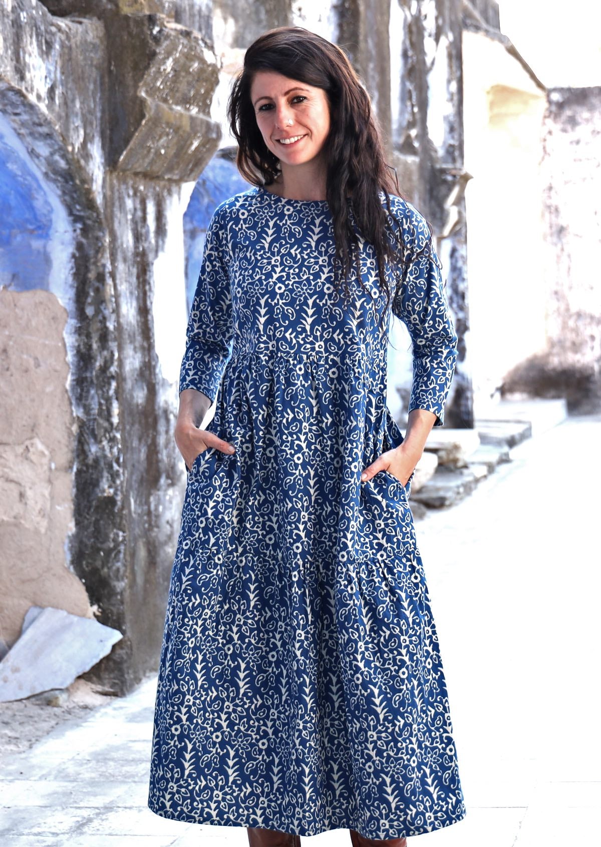 Model with dark hair wearing a relaxed fit blue cotton dress with white floral print and round neckline.