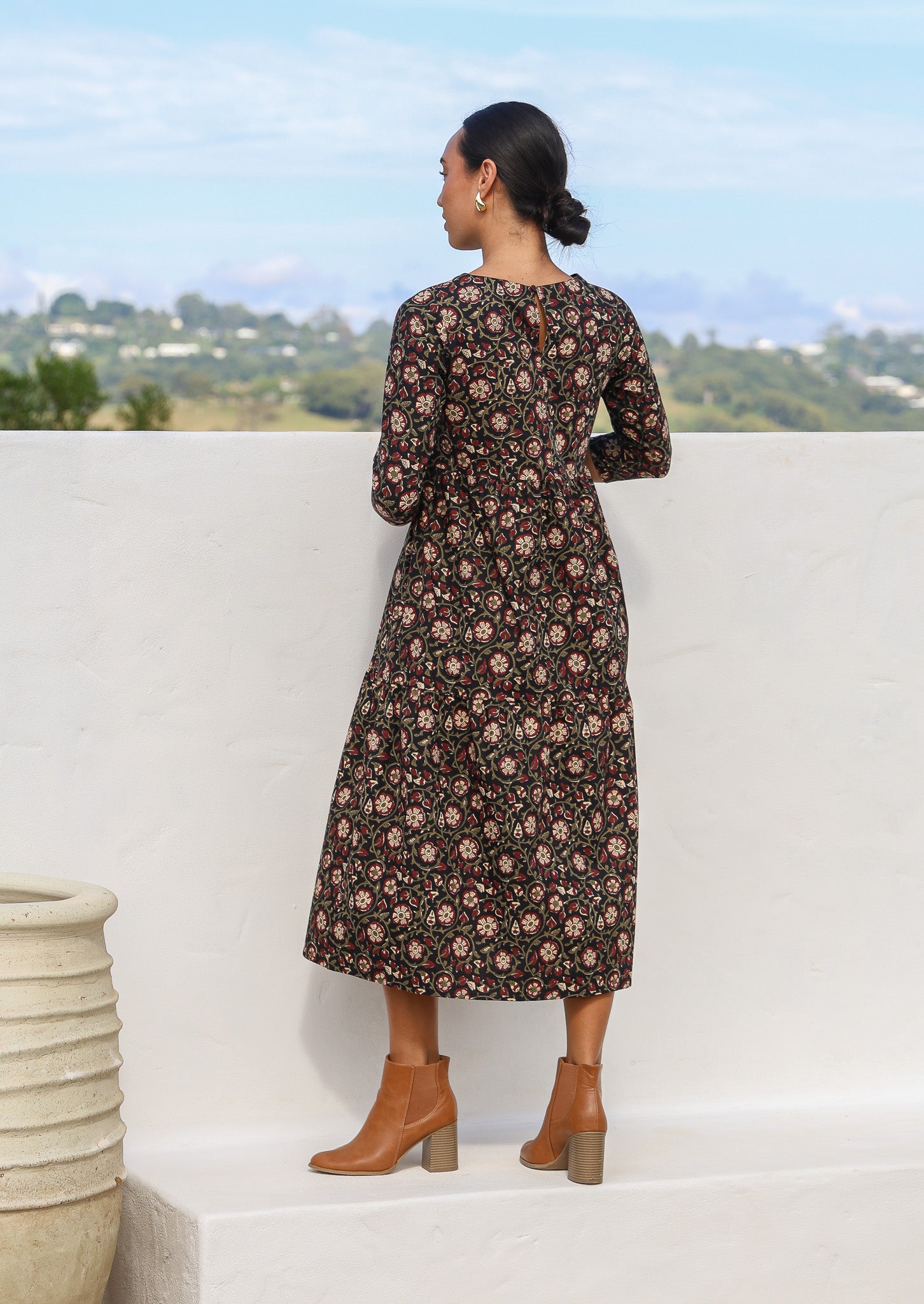 Back pose of model wearing a floral printed black cotton dress with empire waist and keyhole button closure at the back.