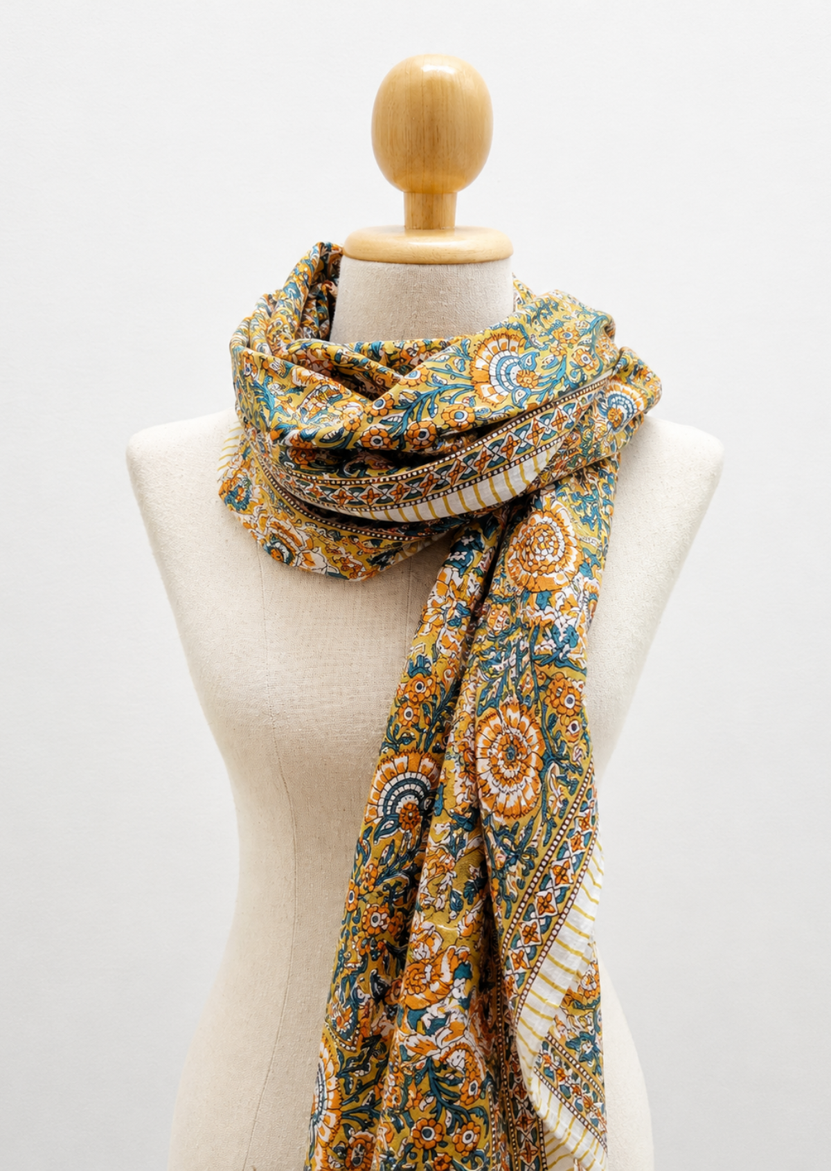A patterned scarf draped on a cream-colored fabric mannequin torso with a wooden neck cap, set against a plain white background.