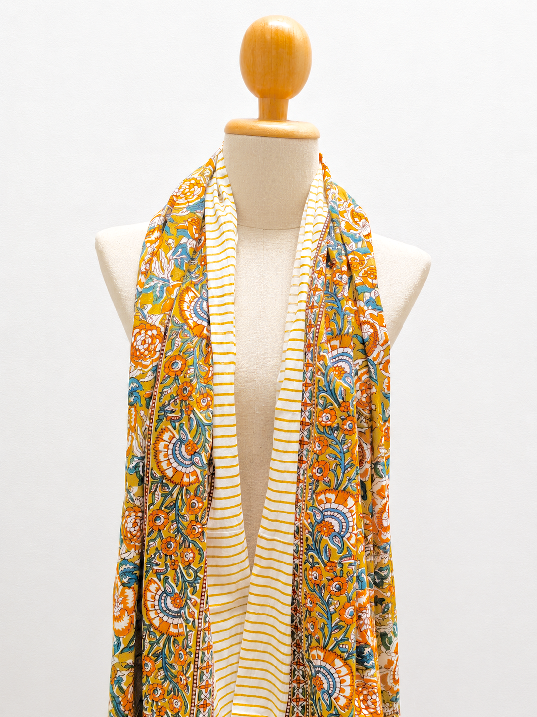 A multicolor patterned scarf draped on a cream-colored mannequin torso with a wooden neck cap, set against a plain white background.