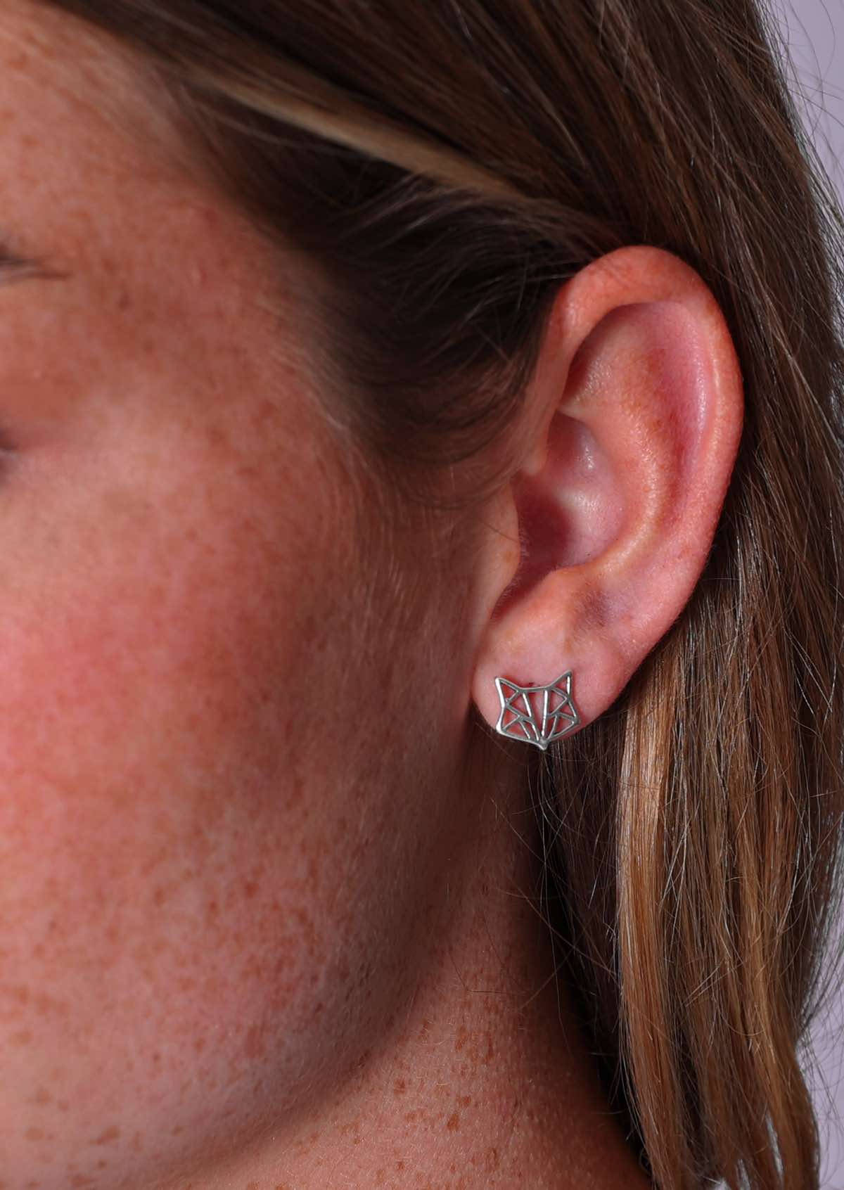 A close-up image of a person wearing sterling silver origami fox stud earrings.