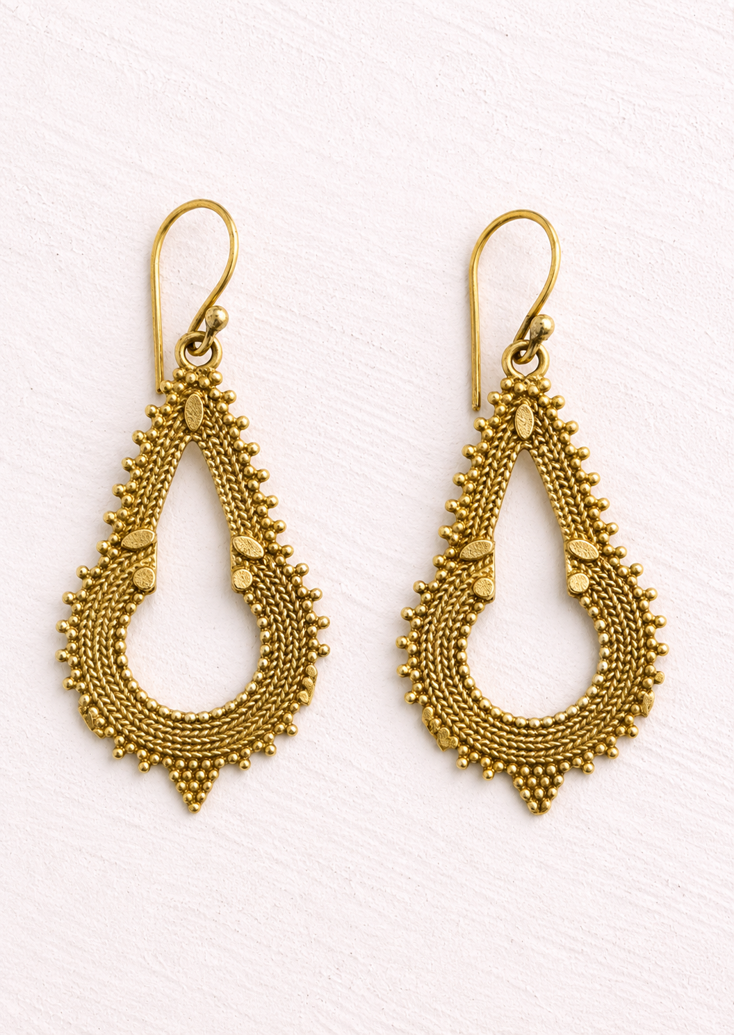Elegant gold coloured teardrop shaped earrings that have layered rope like detailing, tiny raised bead accents, and small leaf motifs inspired by traditional Indian jewellery