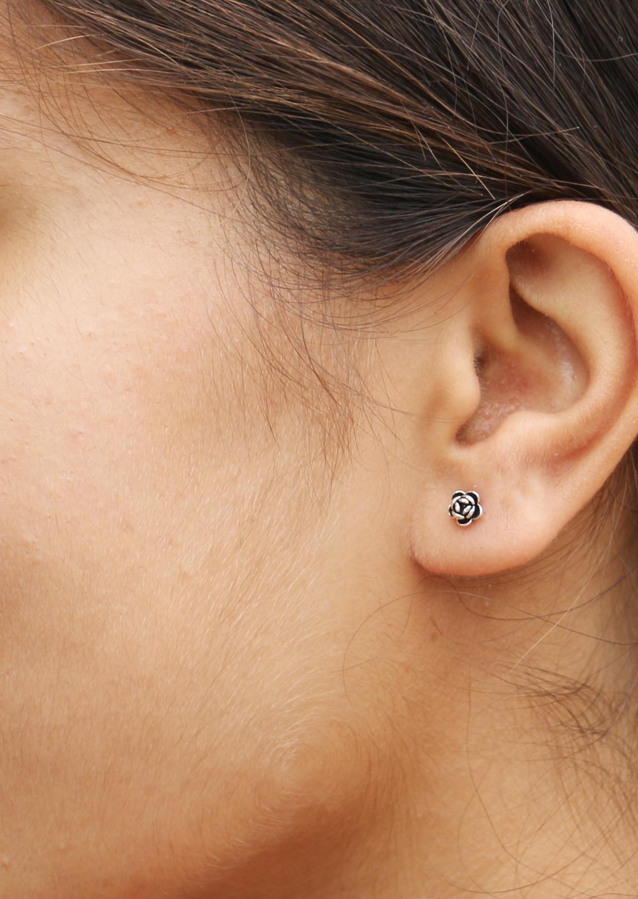 Close-up of an ear wearing a small sterling silver flower petal studs with secure butterfly backs