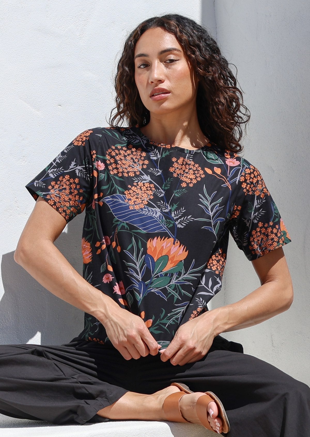 Woman wearing a 100% cotton loose fitting black top with short sleeves, round neckline and button back closure