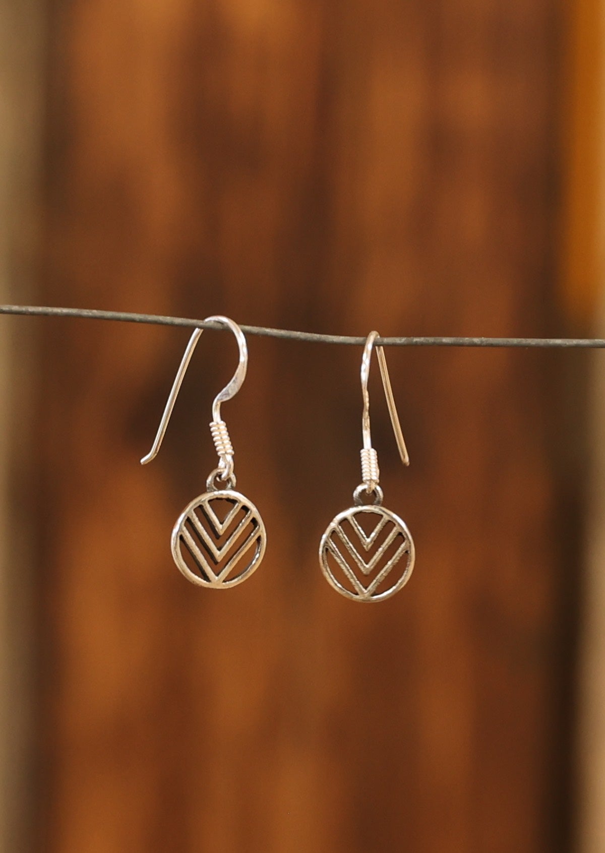 Sterling silver cutout earrings with three 'V's inside a circle, suspended from wire hooks