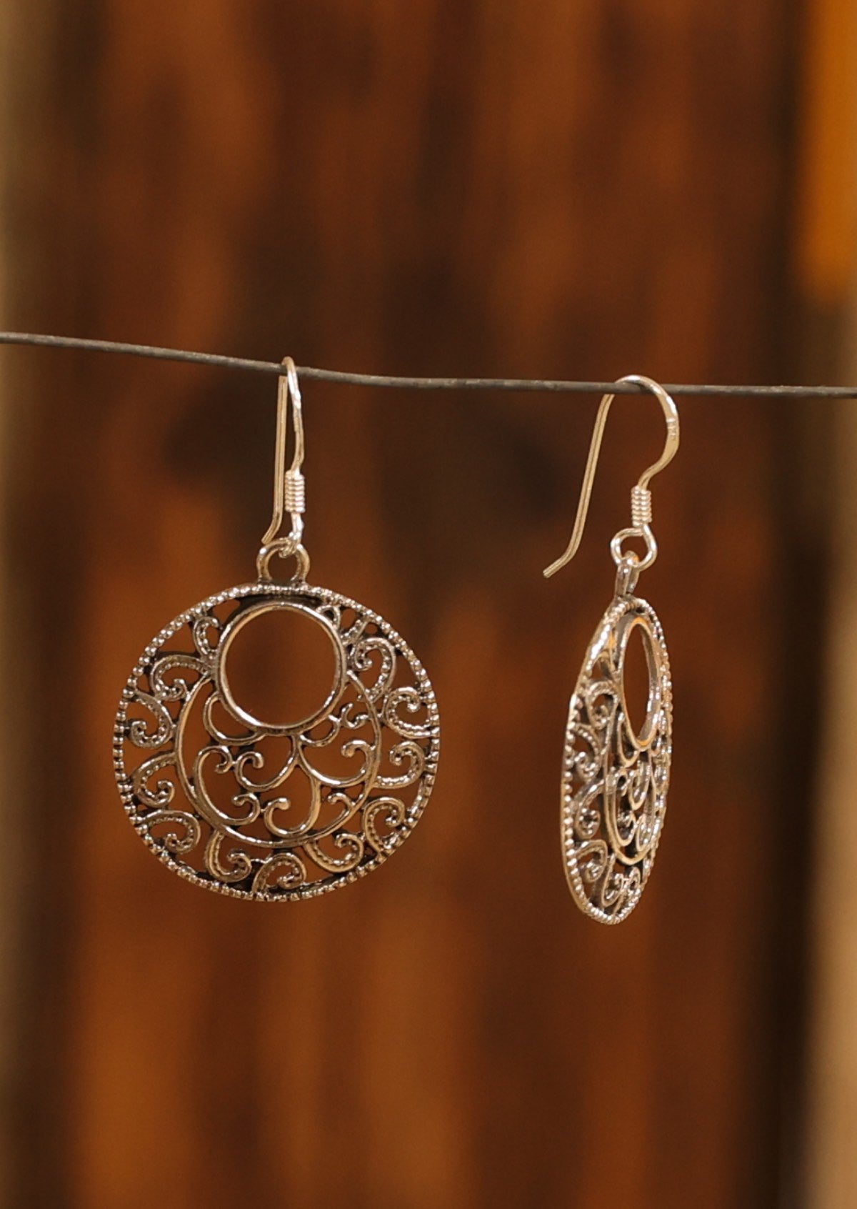 Silver earrings with swirly designs suspended from hooks
