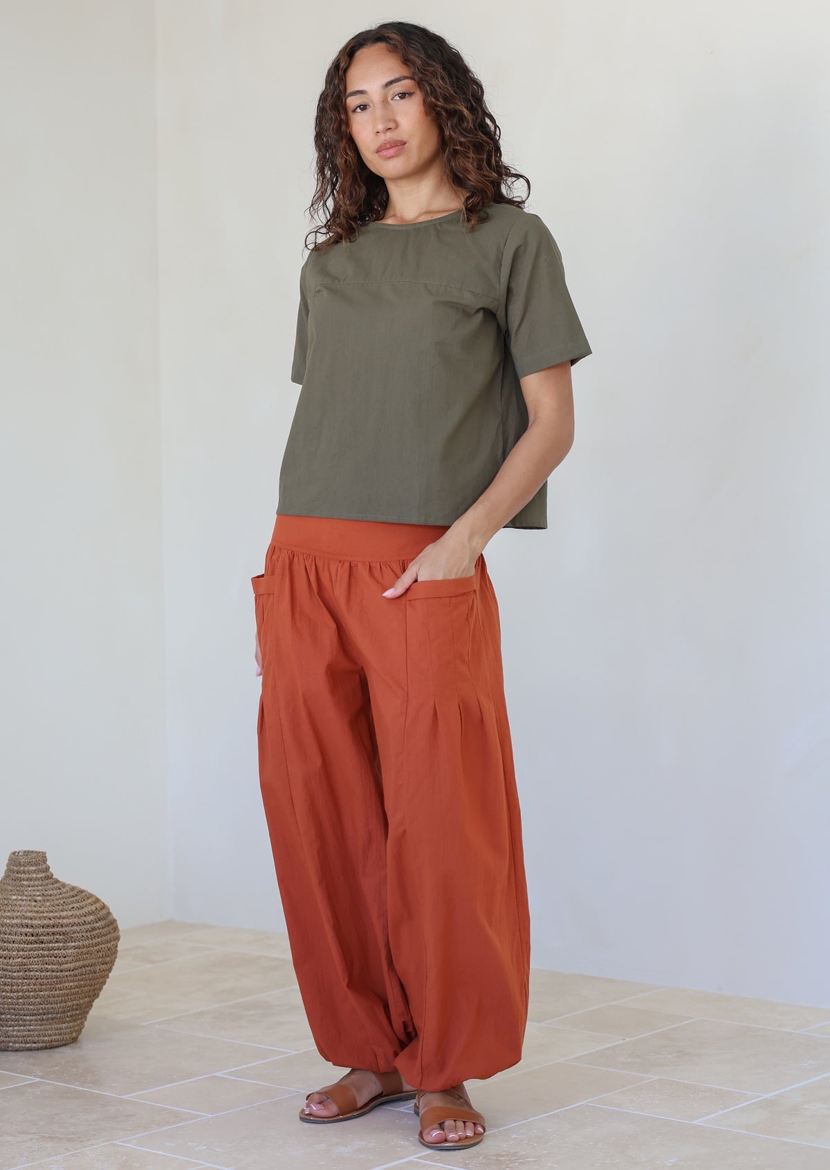 Models poses in rust shade cotton wide leg pants with elasticated ankle