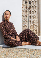 Model in a seated pose pairs floral printed  brown cotton harem pants with a long sleeve cotton tunic.