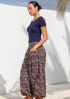 Side pose of model wearing 100% cotton, floral printed deep purple pants with a round neck rayon top.