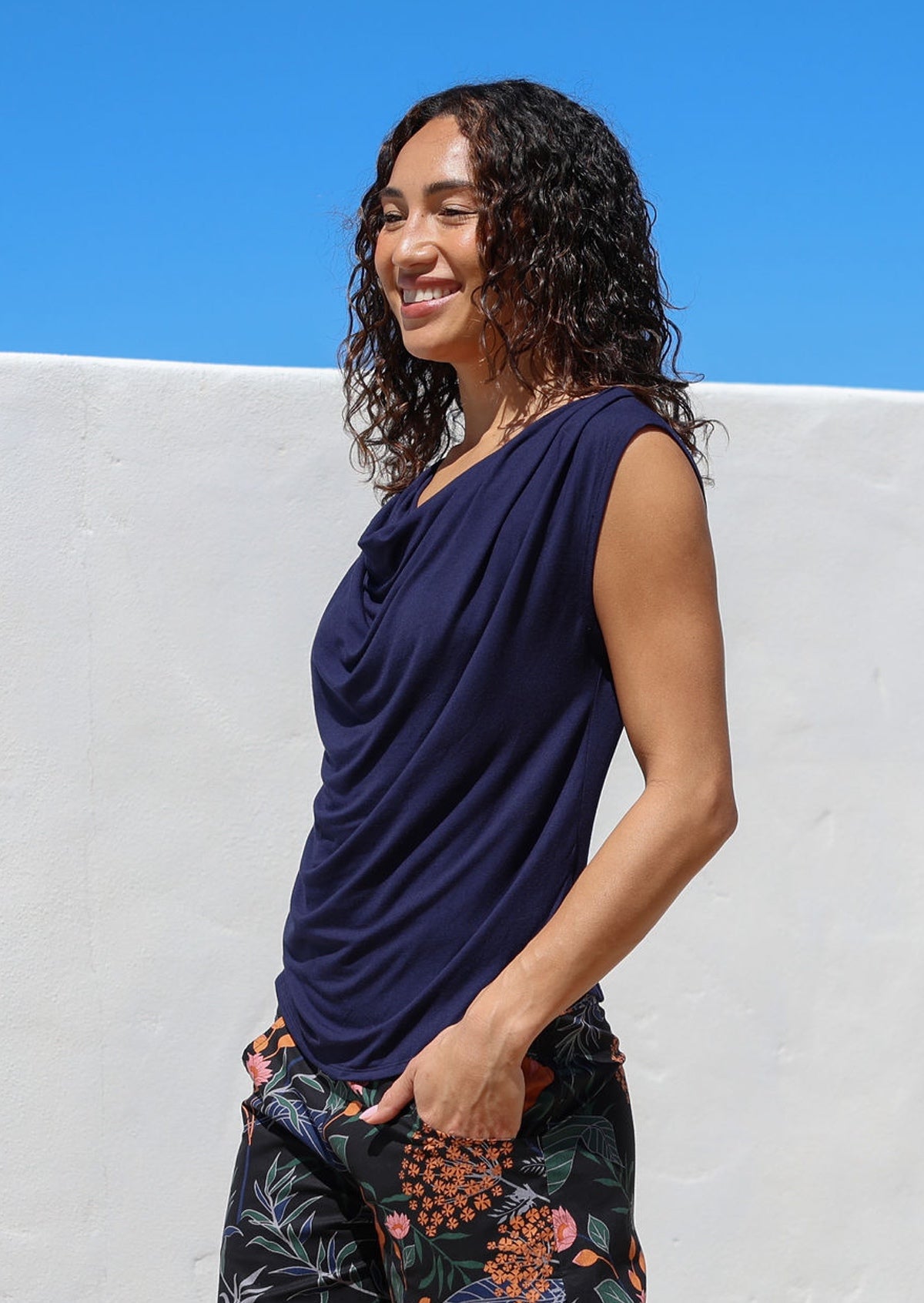 Woman wearing a navy blue sleeveless top with a cowl neckline, paired with dark floral pants