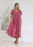 Woman wearing a pink floral Indian cotton maxi dress standing against a white wall.