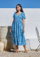 Woman wearing a blue floral cotton maxi dress standing against a white wall with a blue sky.