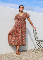 Woman wears 100% cotton button through relaxed fit dress with short sleeves and V-neckline in floral print on a red base