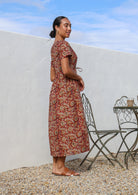 Model posing sideways in a cotton button through relaxed fit shin length dress with V-neckline and T shirt sleeves.