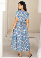Back view of a woman wearing a blue floral cotton dress with gathers at the back, cinched in with thin side ties