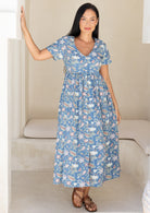 Woman wearing a blue floral cotton midi length relaxed fit dress with short sleeves and a V-neckline and buttons through the centre front
