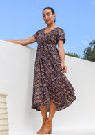 Model standing slightly sideways wearing 100% cotton floral print button through dress with V neck and pockets.