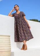 Model standing in sun wearing 100% cotton dark purple button through v-neck dress with pockets and waist tie.