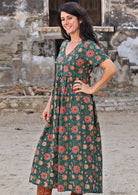 Model standing sideways with hand on waist wearing 100 percent cotton dark jade green button through v-neck dress with pockets