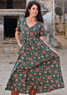 Model holding skirting of dress with one  hand and other hand in pocket wearing 100 percent cotton dark jade green button through v-neck dress