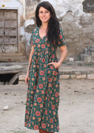 Model standing slightly sideways with one hand in pocket wearing 100 percent cotton dark jade green button through v-neck dress with pockets