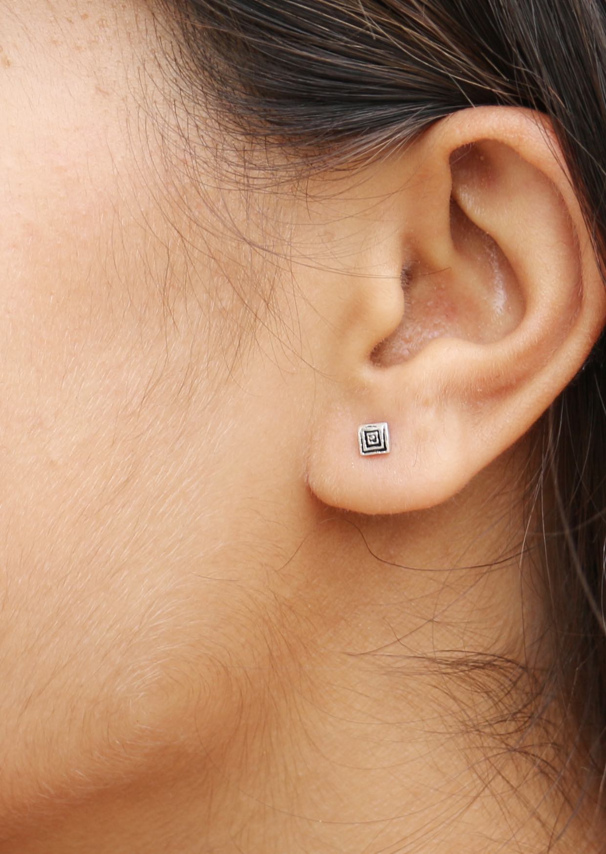 Close-up of woman wearing a small geometric stud earring with polished ripples