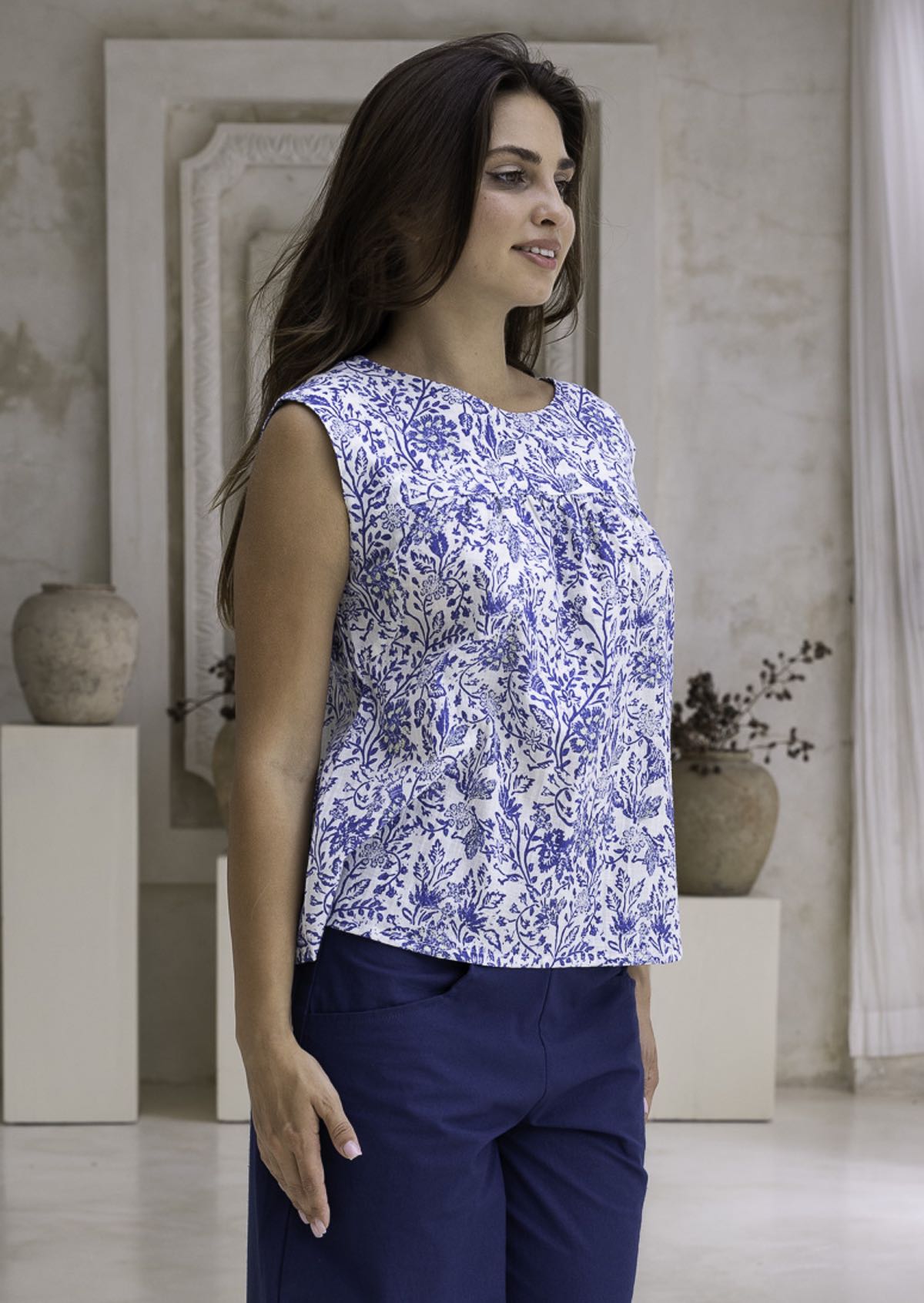 Woman wearing a white based blue floral, 100% cotton top in an indoor setting.