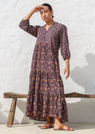 Model wears dark purple based floral cotton dress with pockets, 3/4 sleeves, V neck and mandarin collar.