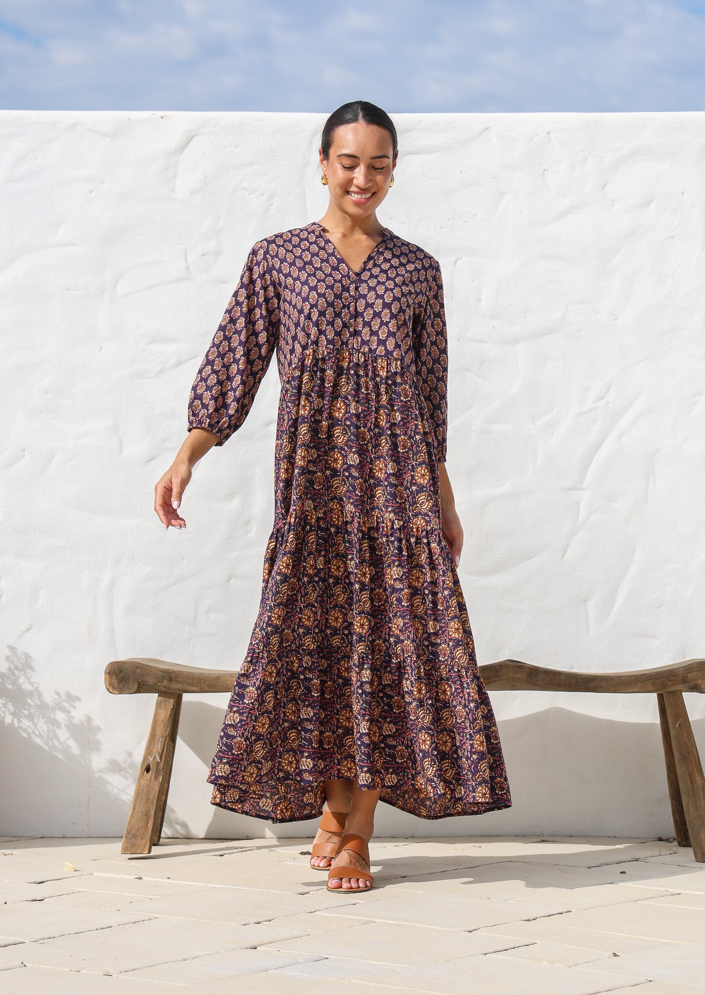 Model wearing a cotton three tiered maxi dress with  3/4 sleeves and buttoned bodice in combination of two purple based floral prints.