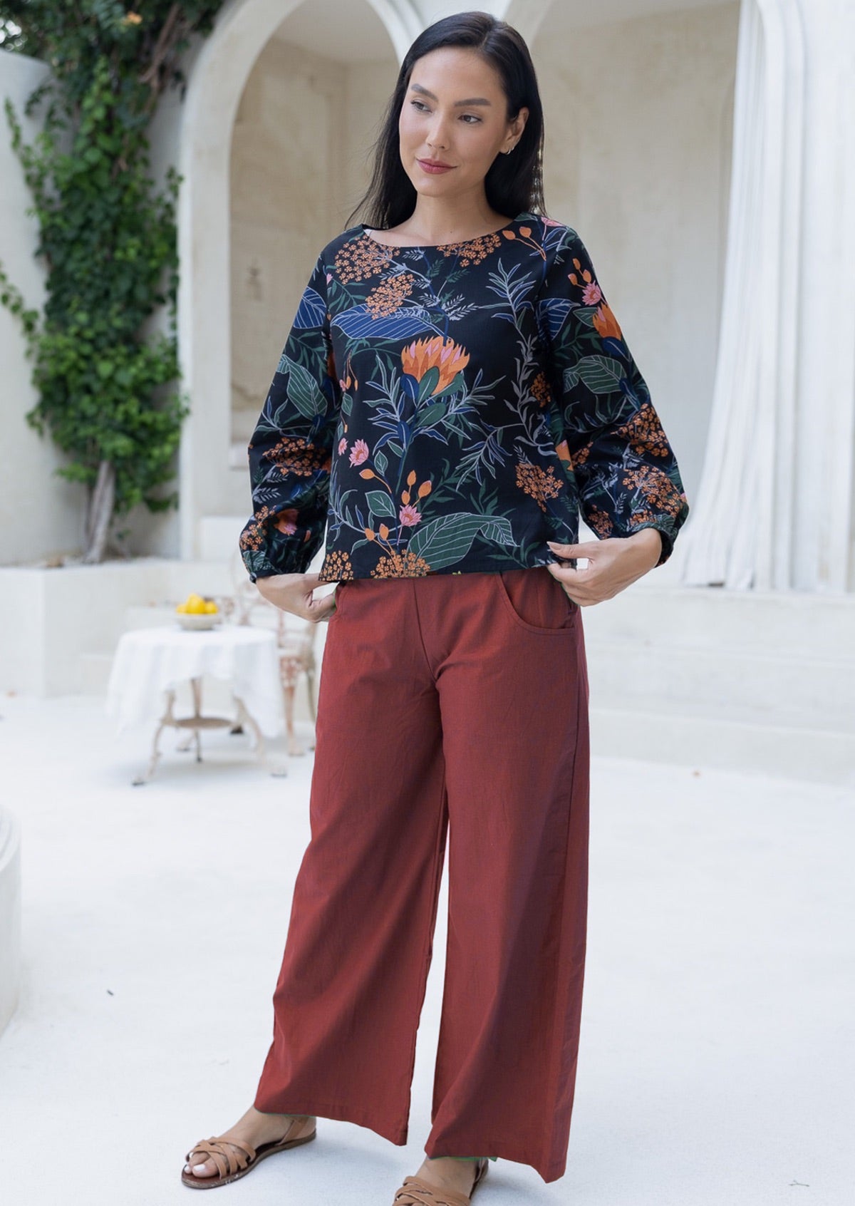 Woman wearing a floral top and red cotton pants standing in an outdoor setting.