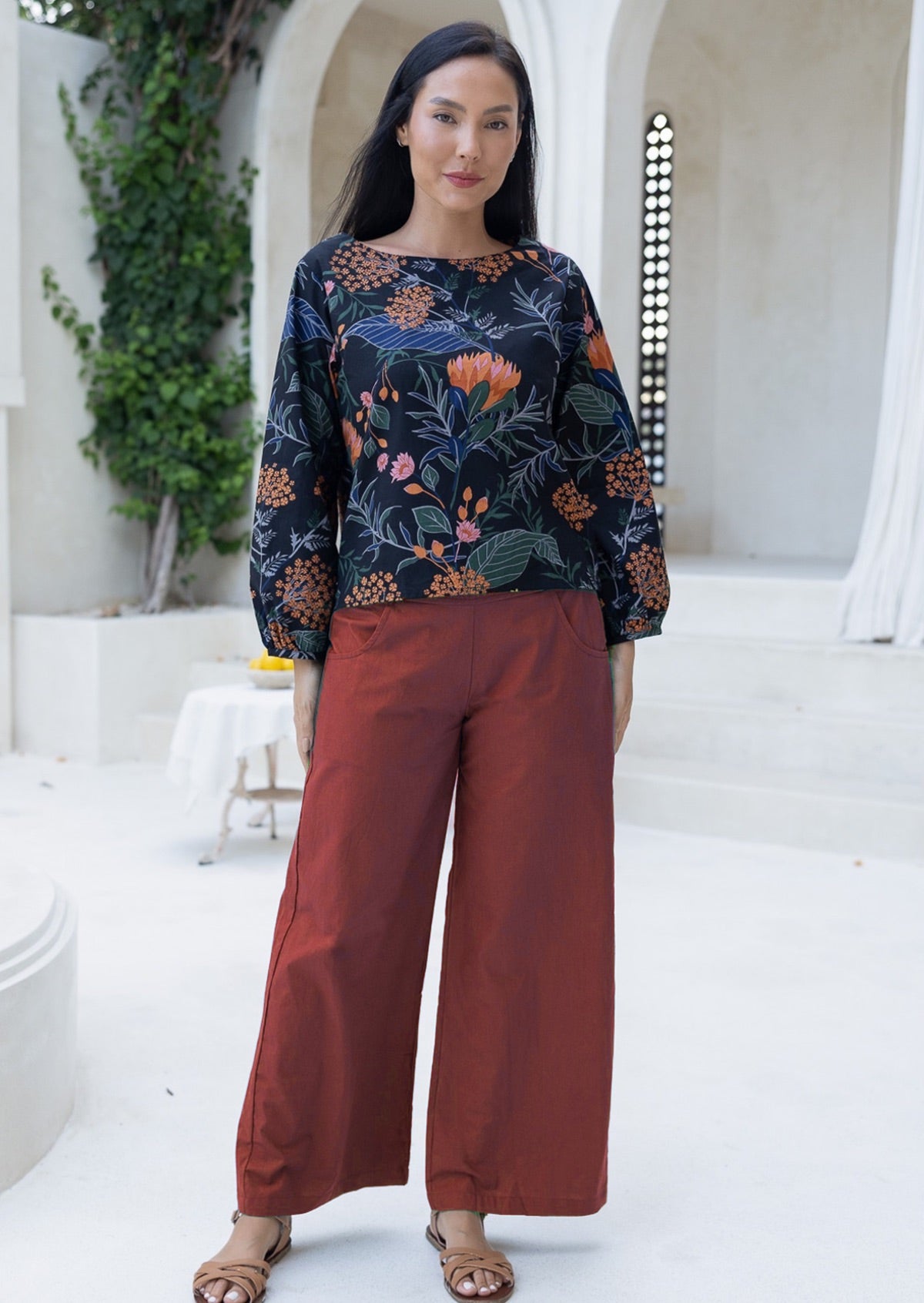 Woman wearing a protea patterned top and red cotton pants standing in a bright outdoor setting.