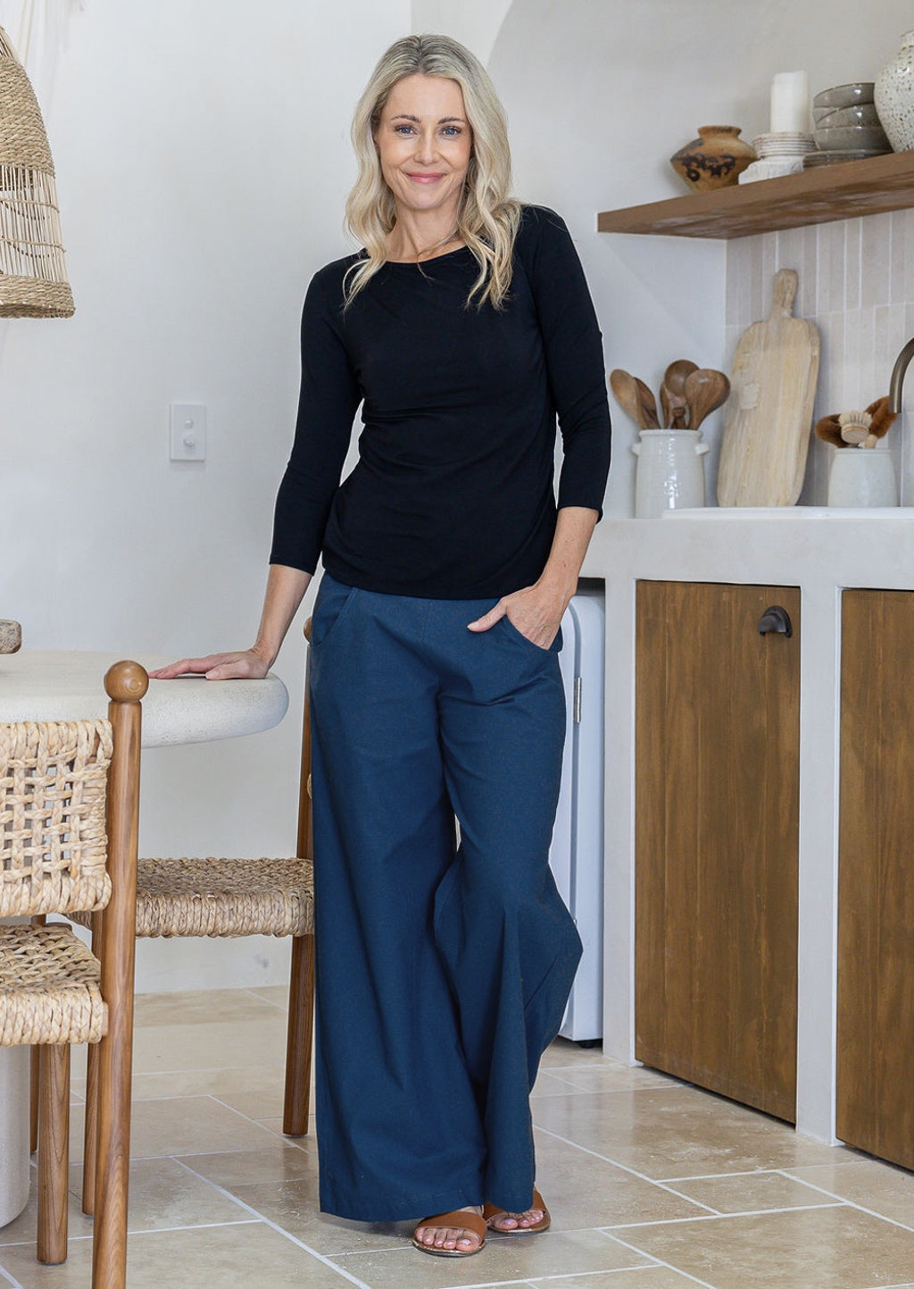 Woman wearing blue cotton wide leg pants paired with a black top, with hand in pocket