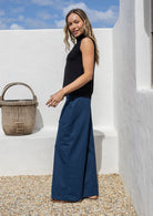 Woman standing sideways wears a deep sea blue cotton pants standing against a white wall with a wicker basket
