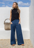 Woman wearing blue cotton wide leg pants with a wide waistband, side zipper, and pockets, standing against a white wall