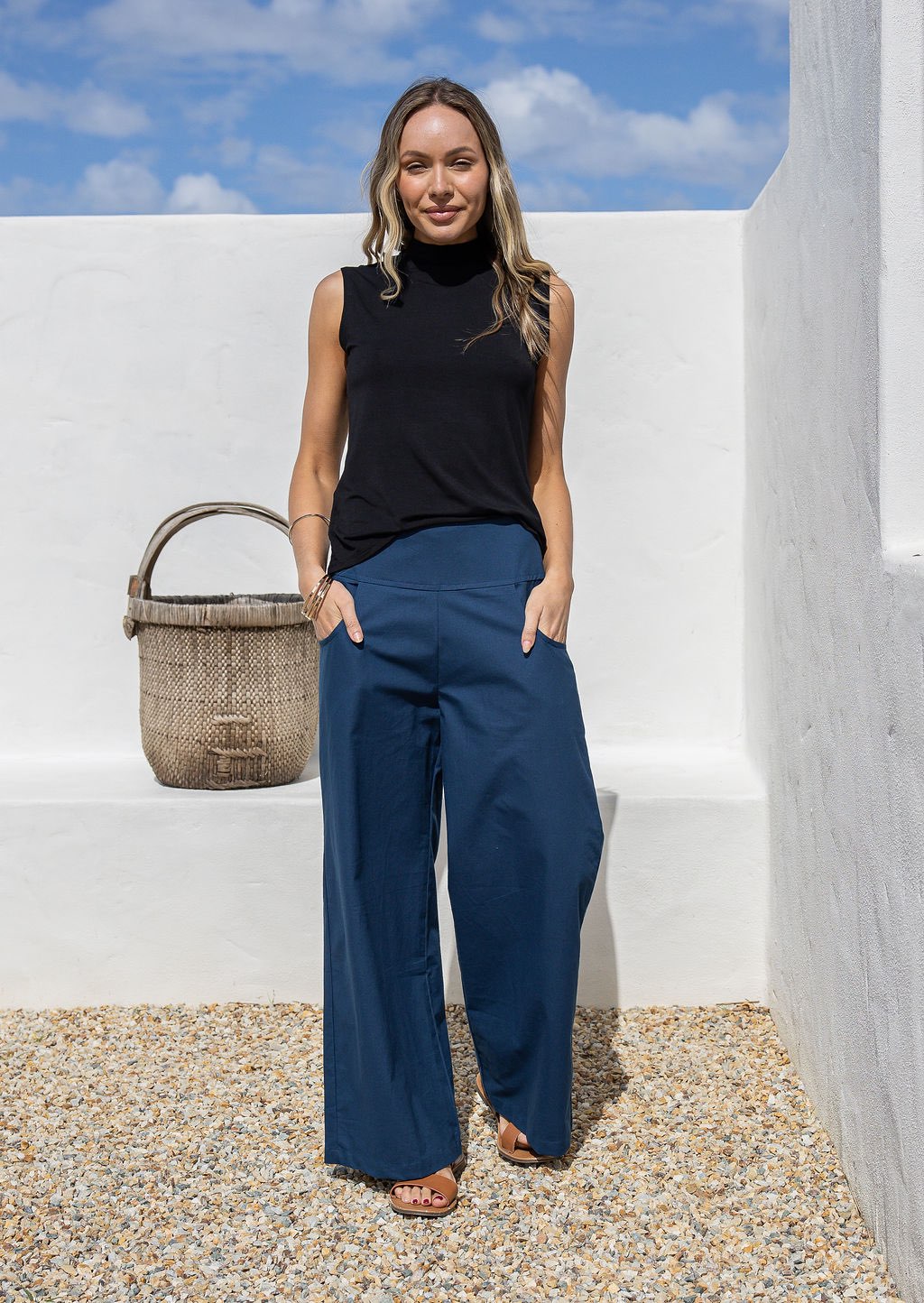 Model standing with hands in pocket wears high waisted, wide leg 100% cotton pants with highneck black rayon top