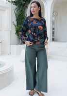 Woman wearing a black based floral top and green wide legged pants in an outdoor setting