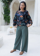 Woman wearing a black based floral top and green wide legged pants