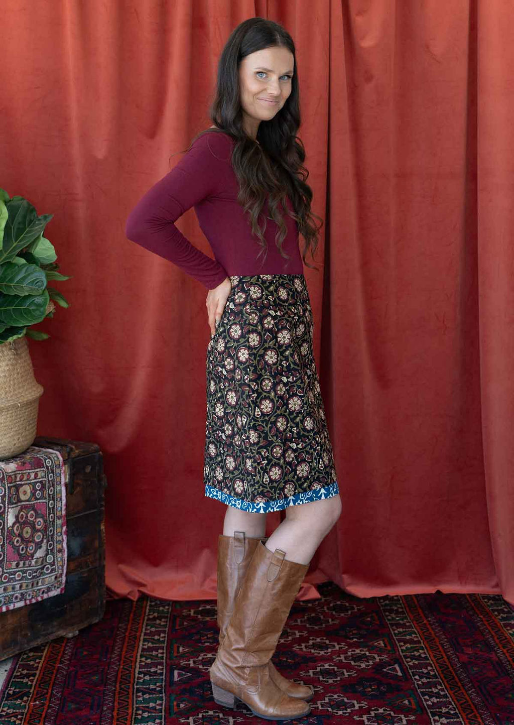 Model standing sideways wears a reversible cotton skirt in bold floral print with the pop of blue band at the base of the skirt.