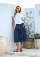 Woman wears dark sea blue cotton skirt with button front, belt loops, box pleats and pockets