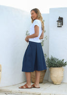 Woman standing in a back pose wearing a 100% cotton knee length A line skirt with belt loops, box pleats, pockets and elastic back waist