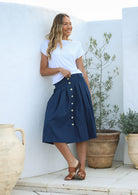 Woman wearing a basic white rayon top and navy A line cotton skirt with box pleats, belt loops and button through front