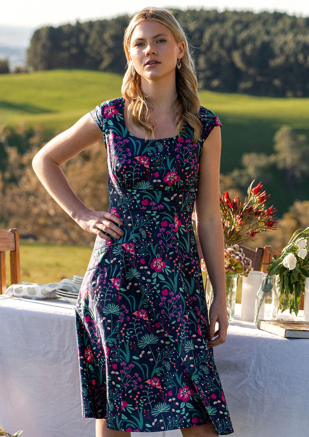 woman in retro inspired Scarlett Dress Dianthus in a  vibrant navy, purple, pink and aqua floral print on 100% cotton in country setting