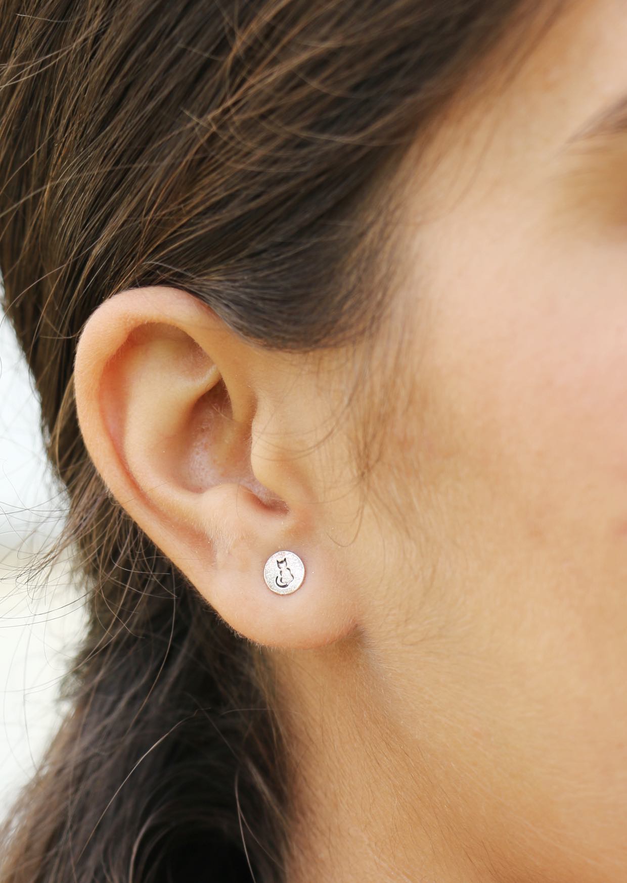 Close-up of an ear wearing a sterling silver small round earring with cat silhouette on the front